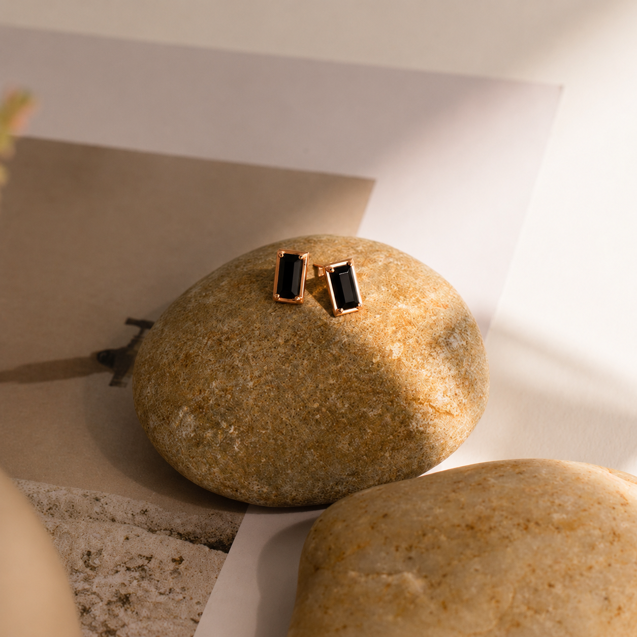Gold square earrings on a stone surface with soft lighting
